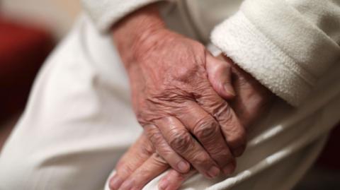A stock of image of an elderly person's hands, crossed on their lap.