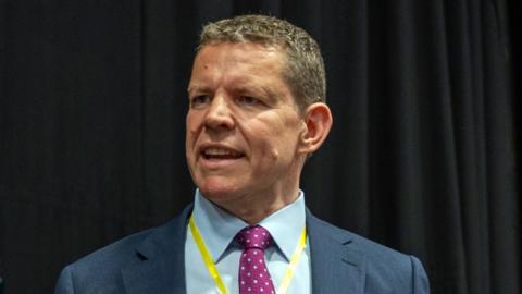 Rhun ap Iorwerth, a man with short brown hair in a blue suit