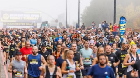 Hundreds of runners set off en masse at the starting point in the fog. Trees line the road to the side.