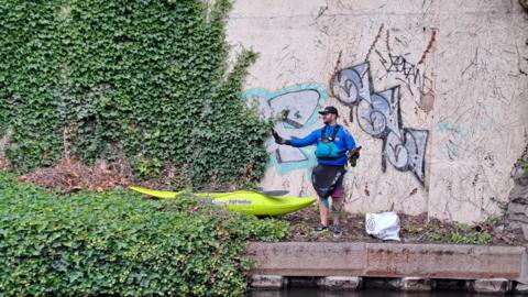 A man stands along the bank of the canal during last year's clean-up with a canoe next to him 