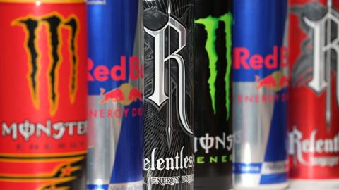 Close up image shows brightly coloured Monster, Red Bull and Relentless energy drinks are displayed on a supermarket shelf. 