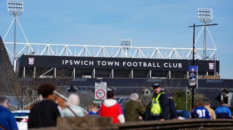 The outside of the Ipswich Town stadium, with a line of fans queuing up outside