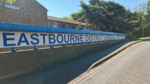 A blue sign outside a hospital that reads Eastbourne District General Hospital. 