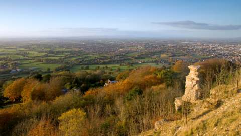 A rock formation called devils chimney on a hillside with a wide landscape beyond including countryside and homes