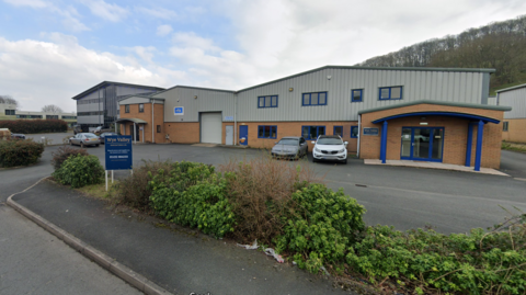 A warehouse/factory building, with several cars in the car park in front. A sign by the entrance reads: "Wye Valley"