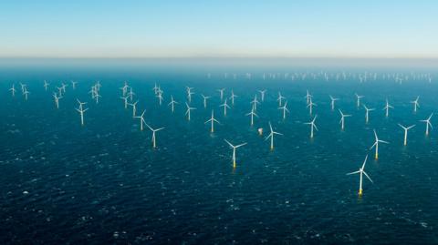 A drone image of a wind farm located in the middle of a sea. Wind turbines are placed in long rows next to each other.