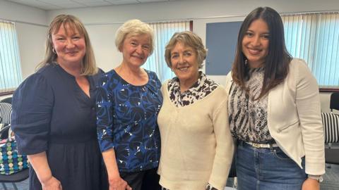 Four women stand together smiling at the camera