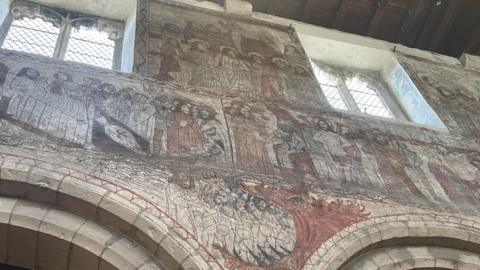 The interior of a church wall with its bricks completely covered by red and black paintings of people.