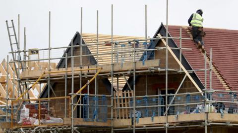 A roofer working on the roof of a new house which has scaffolding around it