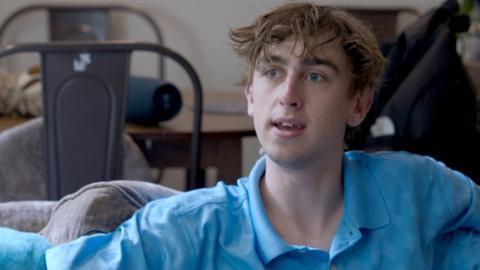 Young man wearing a blue shirt sitting in a living room