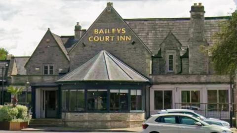 The exterior of Bailey's Court Inn, a pub in Stoke Gifford. The building is grey with a gold sign on the top.