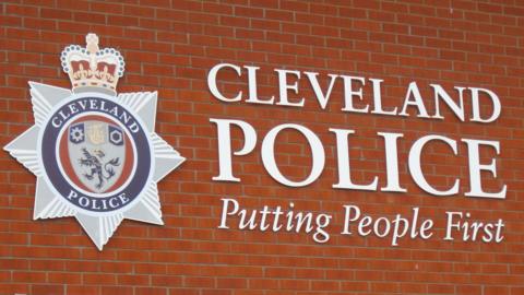 Sign saying "Cleveland Police Putting People First" on a brick wall as well as a Cleveland Police badge