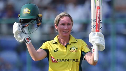 Australia batter Beth Mooney raises her helmet and bat to celebrate hitting a century against India in the third ODI