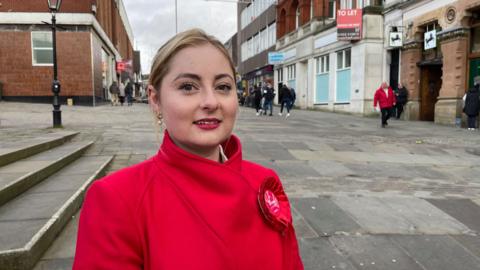 Gen Kitchen wearing a read coat with a red rosette