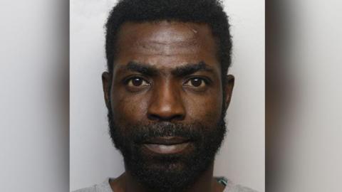 Police custody shot of Hassan Suliman: he has black hair and a beard, and wears a grey t-shirt.