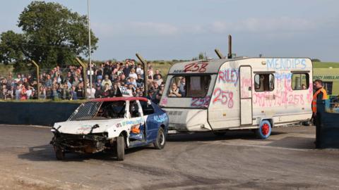 Car and caravan being raced around the track with spectators watching 