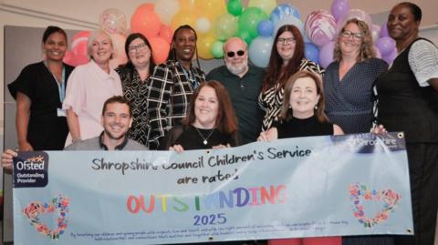 Eleven people stand near a banner saying Shropshire Council Children's Service are rated outstanding 2025.