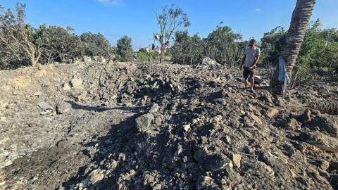 A man stands by a crater left by an overnight Israeli air strike on a house in the area of Burj al-Shamali, near Tyre, southern Lebanon (6 August 2026)