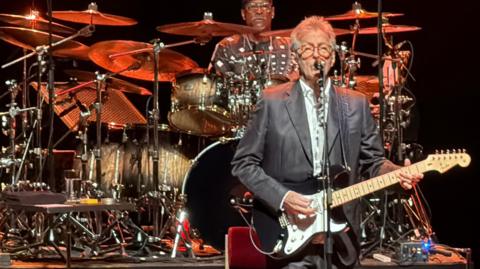 A man, Eric Clapton, stood holding a guitar while performing on a stage.