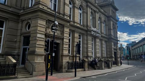 A sandy-coloured brick building, is pictured on a mild day. 'Bradford Arts Centre' is written on the front of it in silver letters.