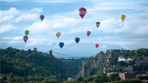 Eleven hot-air balloons flying above Clifton Suspension Bridge on a sunny day