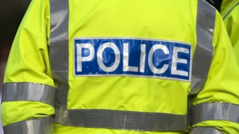 The back of a police officer's uniform. It is yellow in colour and reads 'Police'.