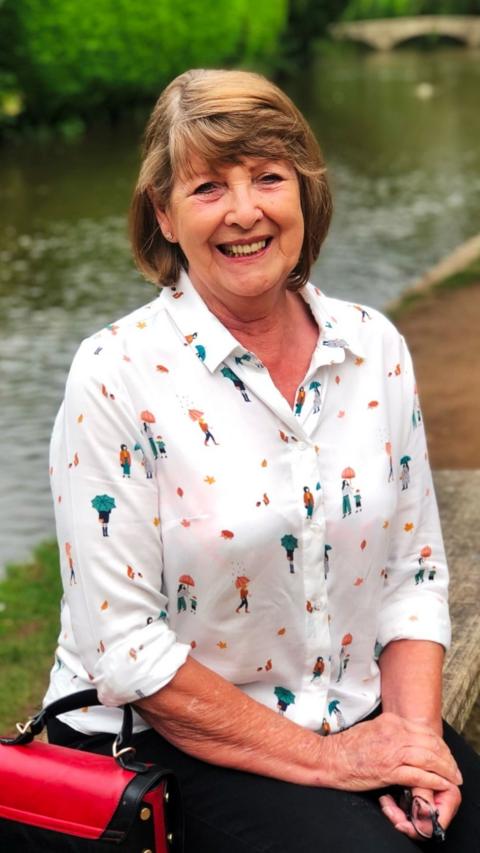 Barbara is sitting by a canal wearing a white shirt and smiling at the camera.