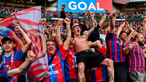 Crystal Palace fans celebrating in the stands at Wembley with the words goal on a large screen behind them