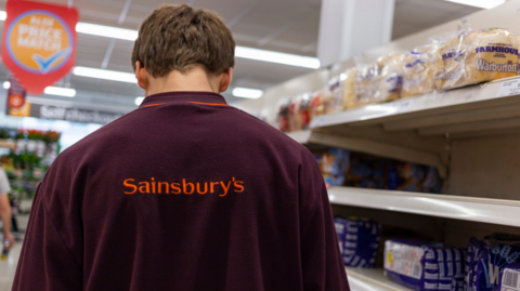 Sainsbury's worker standing next to bread on shelves 