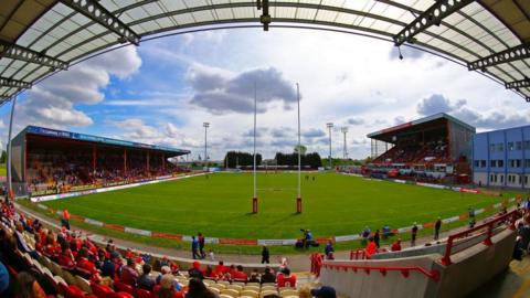 A generic image of the stadium from inside the ground. There are fans sitting in all the stands. It is a sunny day. There are no players on the pitch as the match hasn't started.