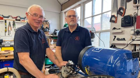 Two men in blue shirts fixing a machine in a workshop