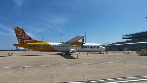 An Aurigny plane at Guernsey Airport. It is yellow and white. 