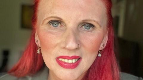 A close up picture of Bridget Chapman, she has red hair and two sets of earrings in. She has a gold nose ring and blue eyes.