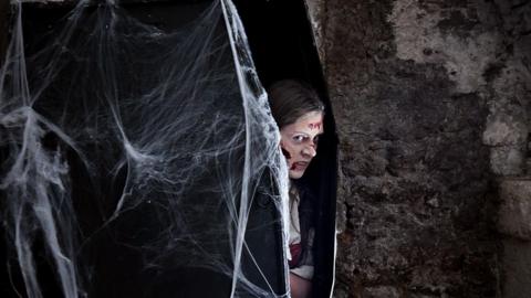 Student dressed up as a zombie coming out of a coffin with cobwebs on it