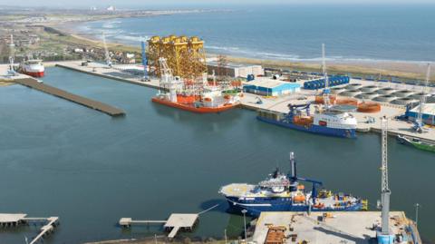 An aerial view of the port of Blyth with a number of docks visible and ships moored up. Beyond the port the coast stretches out.