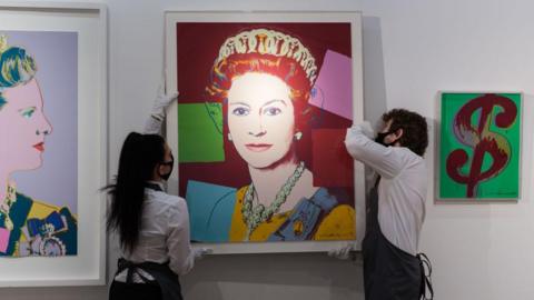 Two people hang an artwork depicting Queen Elizabeth II