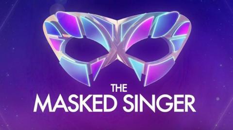 The logo for the TV show The Masked Singer. It is a multi coloured eye masked on a purple background with the words 'The Masked Singer' below