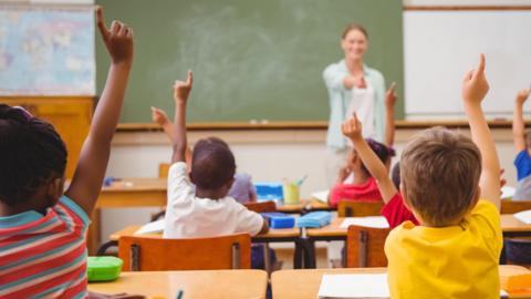 Children with their hands up in a classroom