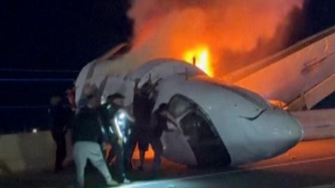 Wreckage of jet and multiple bystanders are in the image, helping pull people from the plane. 