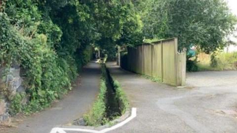 A narrow stream edge with greener runs between two paved tracks.