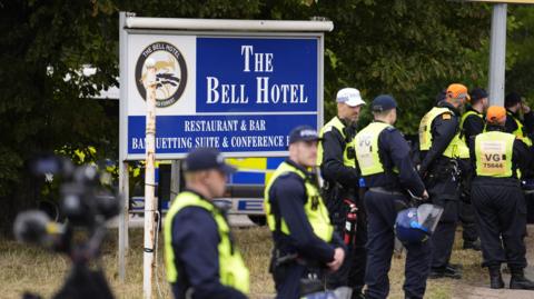 A group of police in high-vis vests stand outside a sign for The Bell Hotel in Epping.