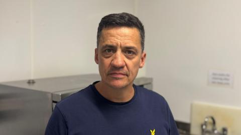 A man in a navy blue top standing in a kitchen.