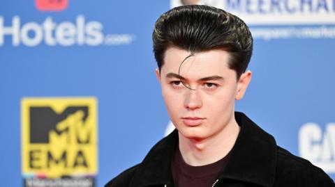 Elliot James Reay poses for photographers against a blue branded backdrop at the MTV Europe Music Awards in Manchester in 2024.