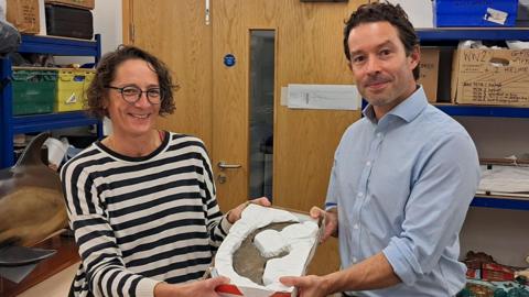 A wide shot of a woman and Xavier Duffy holding the astrolabe.