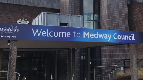 An external picture of Medway Council's premises. The signage reads 'Welcome to Medway Council', to the left of which is a slogan which reads 'Medway Council - Serving You'.