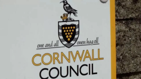 A large white sign for Cornwall Council, including the council logo and motto, "one and all", written in both English and Cornish