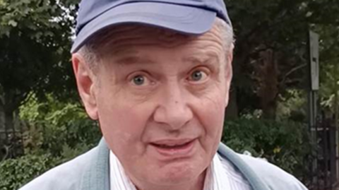 A man wearing a blue cap, white and red striped shirt and blue-grey jacket