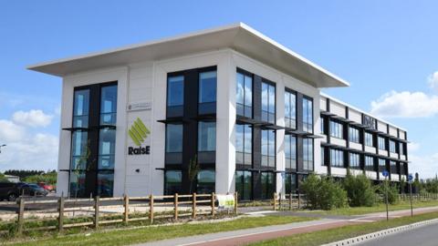 An East Yorkshire business advice centre, a white three storey building with a flat roof and large black windows and wooden fencing and trees in the foreground