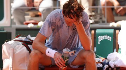 Jannik Sinner sits down in his chair and pours water over his head