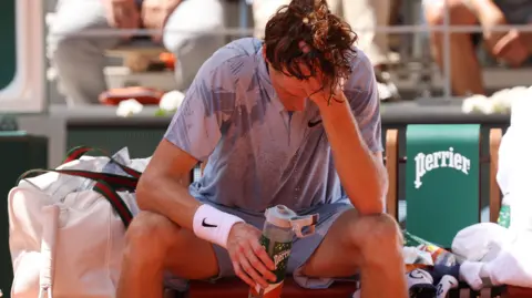 Jannik Sinner sits down in his chair and pours water over his head